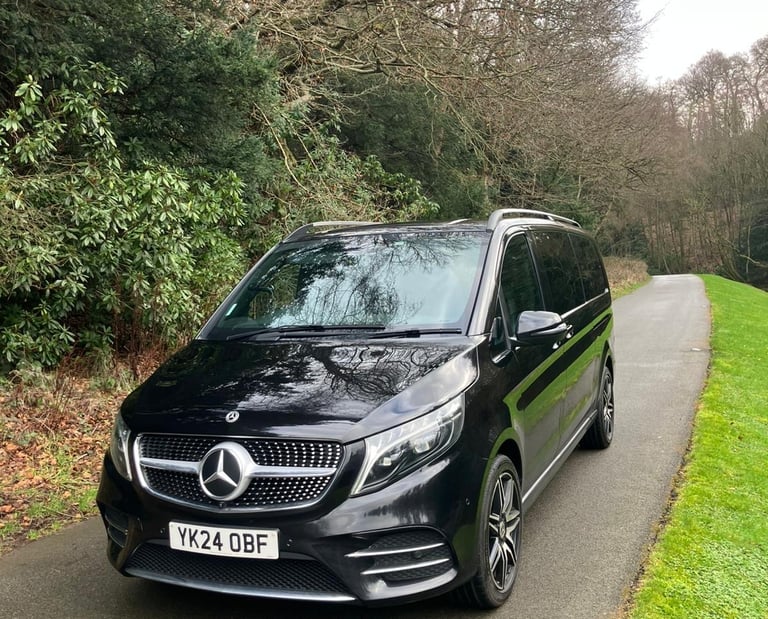 Black Mercedes-Benz V-Class luxury passenger car on a scenic rural road near woodland.