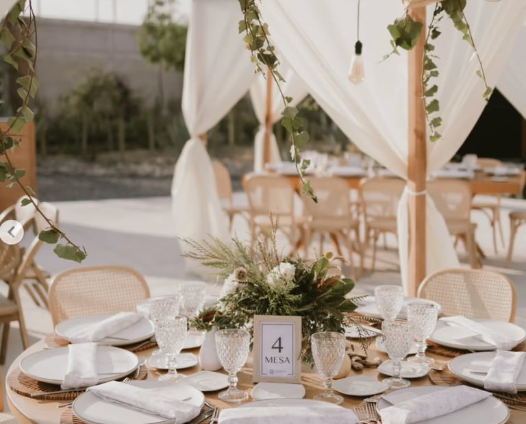 Mesa redonda decorada con vajilla blanca y detalles en madera.