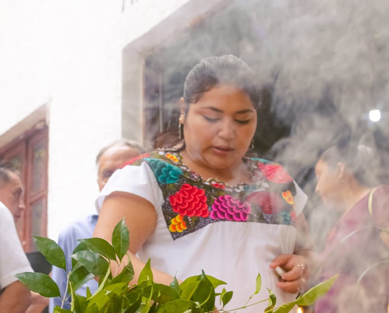 Una mujer con una blusa tradicional mexicana bordada realiza una ceremonia de limpieza con humo 