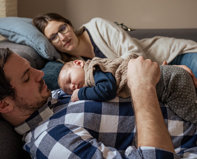 Baby liegt auf dem Papa, die Mama betrachtet die beiden