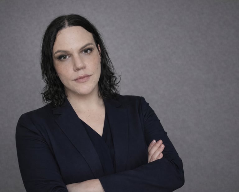 Professional portrait of a businesswoman in a dark navy blazer with arms crossed against a grey background.