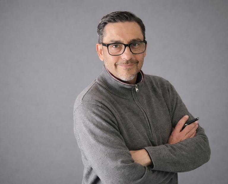 Professional portrait of a man with glasses wearing a grey quarter-zip sweater against a grey background.