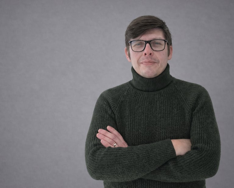 Professional portrait of a man wearing glasses and a dark green turtleneck sweater.