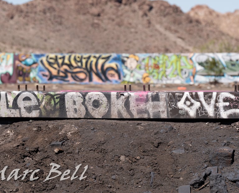 Street art graffiti on concrete barriers in a desert landscape with mountains in the background.