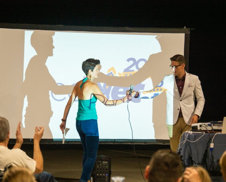 Two people exchanging a microphone in front of a screen