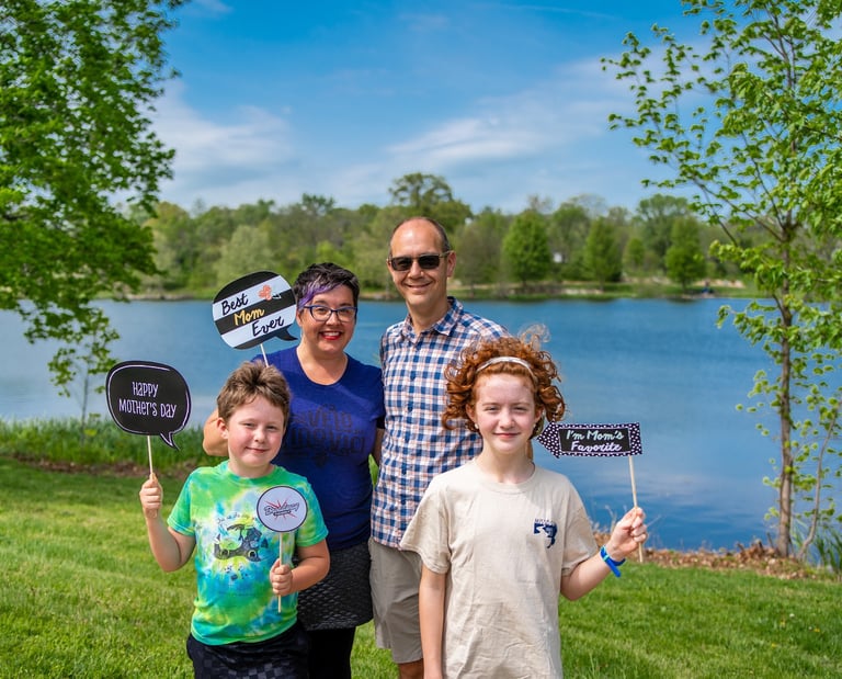 Two parents and two children posing in front of a lake holding sign props