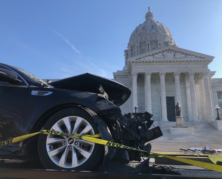 The front of a car that has been in a wreck, with the Missouri capital building in the background