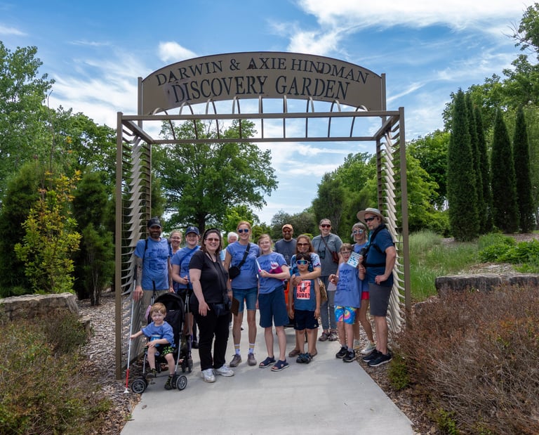 Group photo of adults and children posed on a paved walkway under an entry to a garden