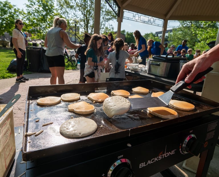 A hand flipping pancakes with a spatula, with people in the background