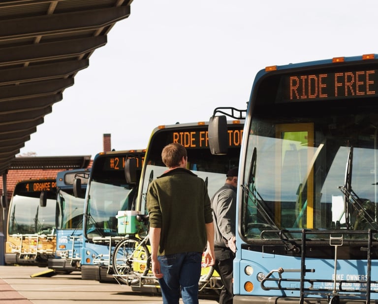 Man walking in front of a line of buses with the bus route sign reading "Ride Free Today"