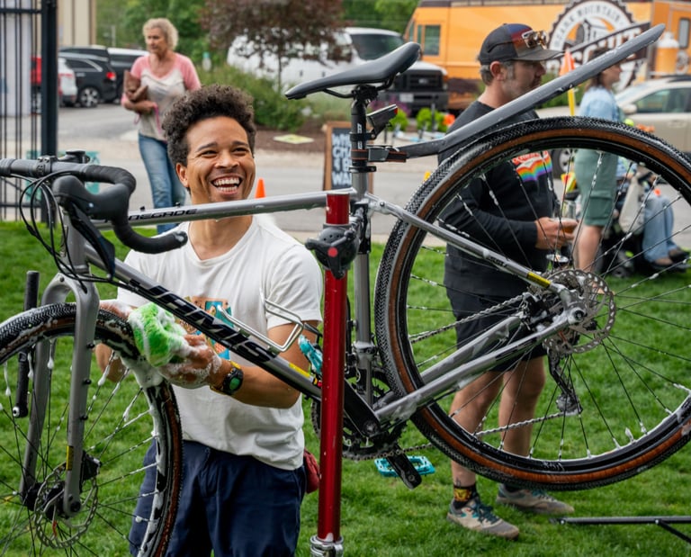 A young man smiling and washing a bike held high on a stand
