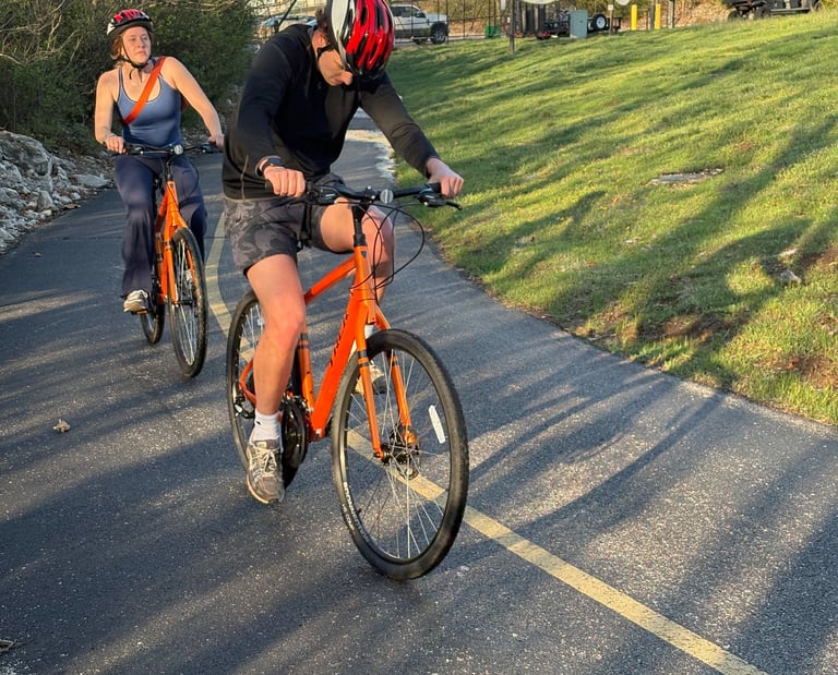 Two people on orange bikes on a paved trail
