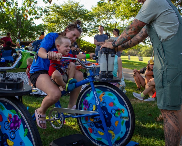 A little kid and a parent powering a smoothie on our blender bike