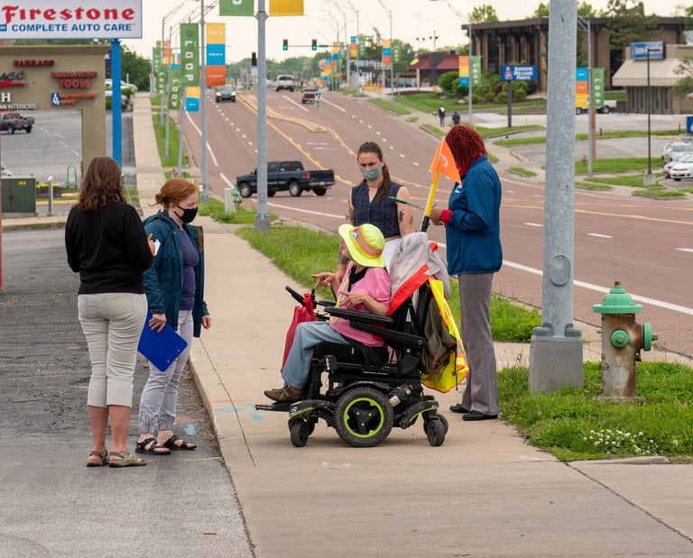 Group gathered on the sidewalk of a busy street