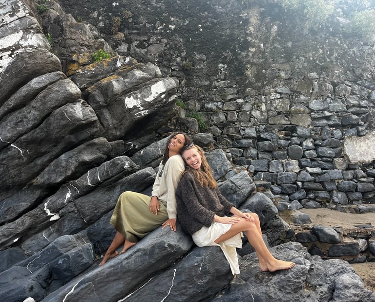 Two women sitting back to back on a rock.