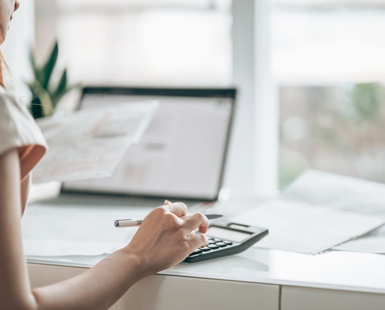 Woman managing monthly bookkeeping, using a calculator and computer to organize financial records.