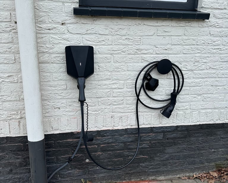Black wall-mounted electric vehicle charging station and cable installed on a white brick house exterior.