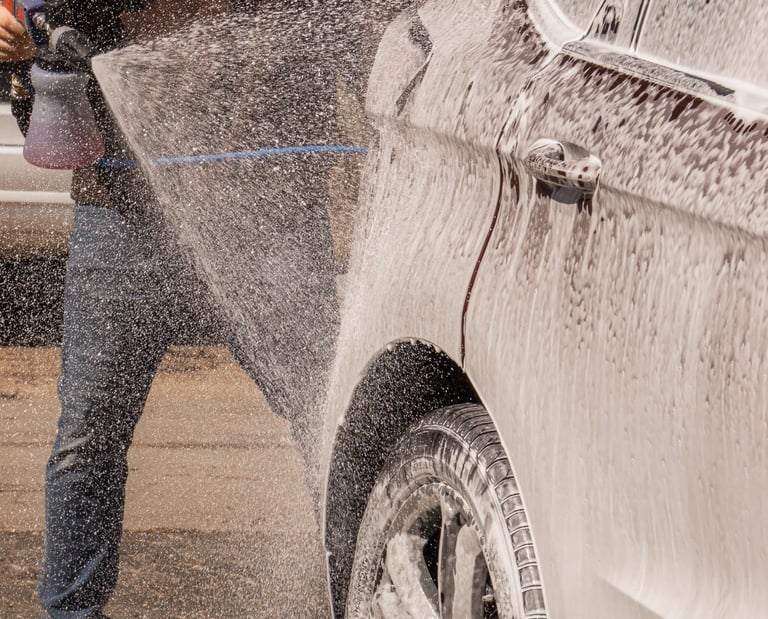 A man uses a high-pressure foam cannon to apply thick car wash soap to a vehicle.