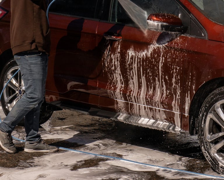 A man uses a pressure washer to rinse soap off a red SUV during a professional car wash service.