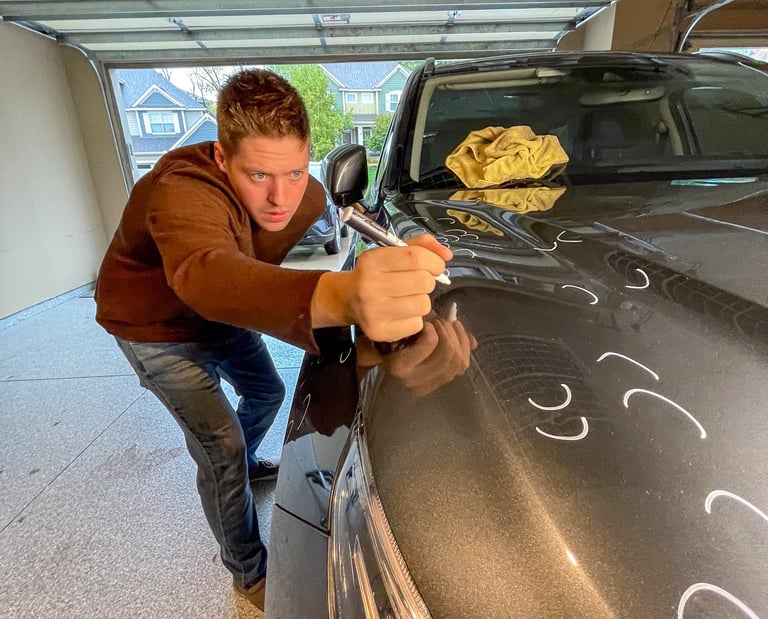 PDR tech marking hail on a hood of a gray SUV vehicle.
