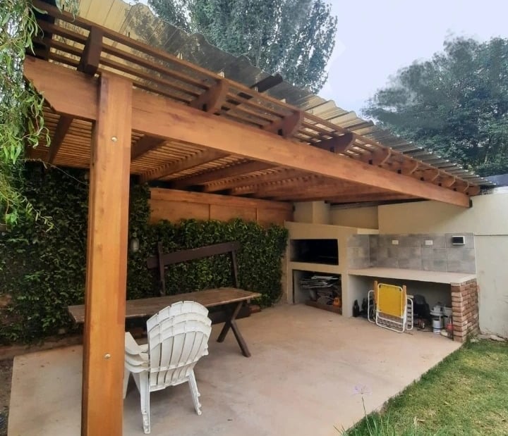 Patio rústico al aire libre con pérgola de madera con techo de chapa ondulada.