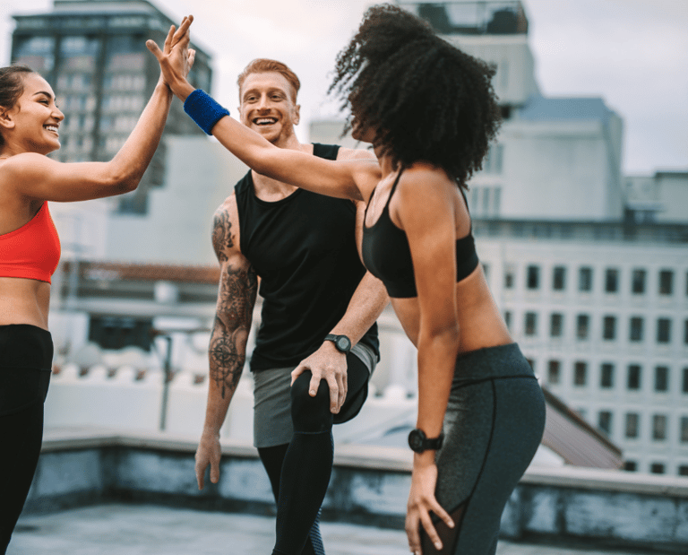 Smiling diverse friends giving high-fives during a rooftop outdoor workout session in the city.