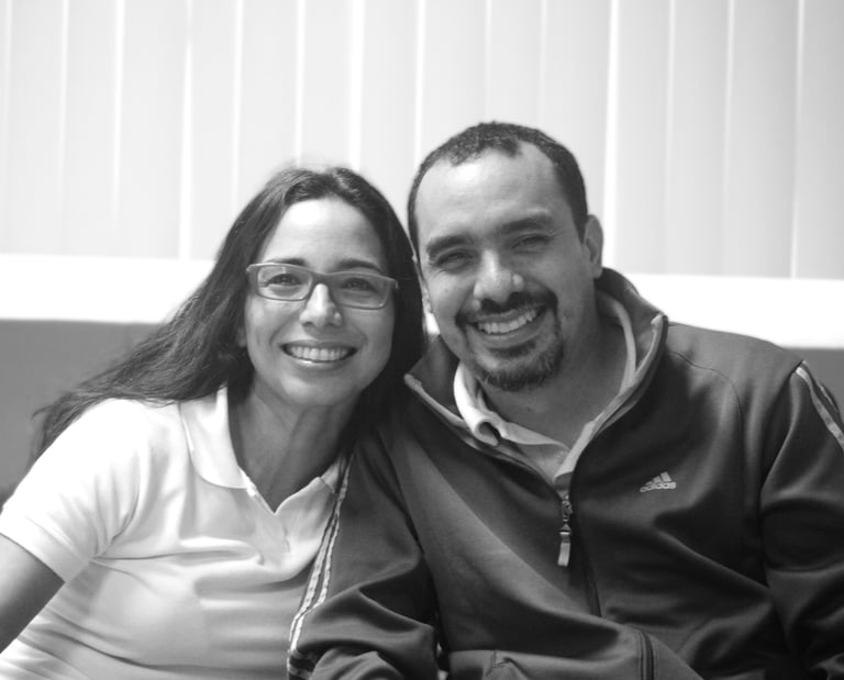 Un hombre y una mujer sentados uno junto al otro en un sofá, sonrientes miran la cámara