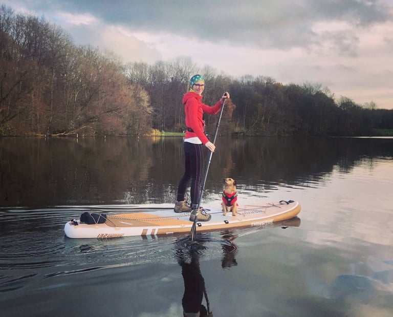 Rita Dekšnytė paddleboarding on a calm lake with her dog