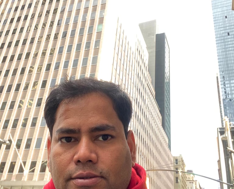 A man in a red hoodie and black jacket taking a selfie among tall skyscrapers in New York City.