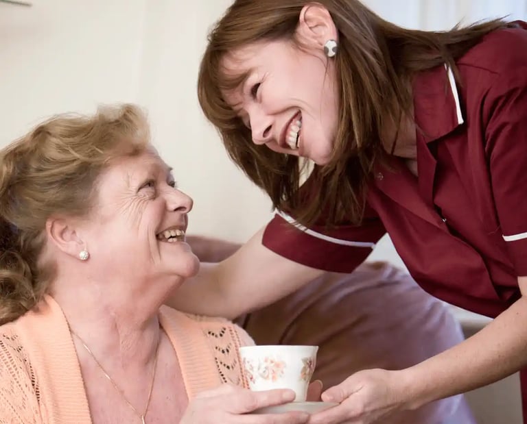 AMG Nurse in red scrubs giving patient a cup of tea