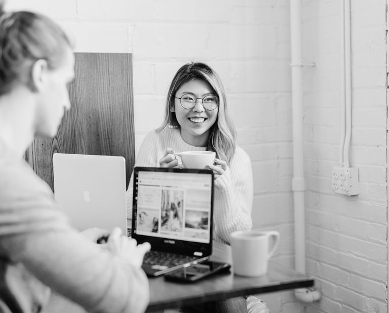 university students sitting at a desk working on their laptops and drinking coffee