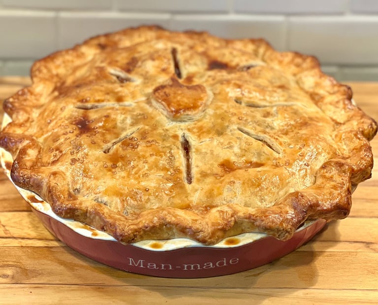 Freshly baked golden brown apple pie with a flaky lattice crust in a red ceramic dish.