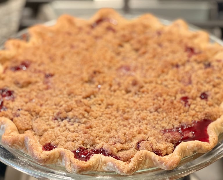 Freshly baked cherry crumble pie with a fluted golden crust and sweet streusel topping in a glass dish.