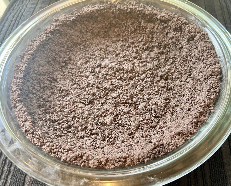 Homemade chocolate cookie pie crust pressed into a clear glass baking dish.