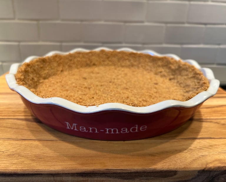 A homemade graham cracker pie crust pressed into a red ceramic pie dish on a wooden cutting board.
