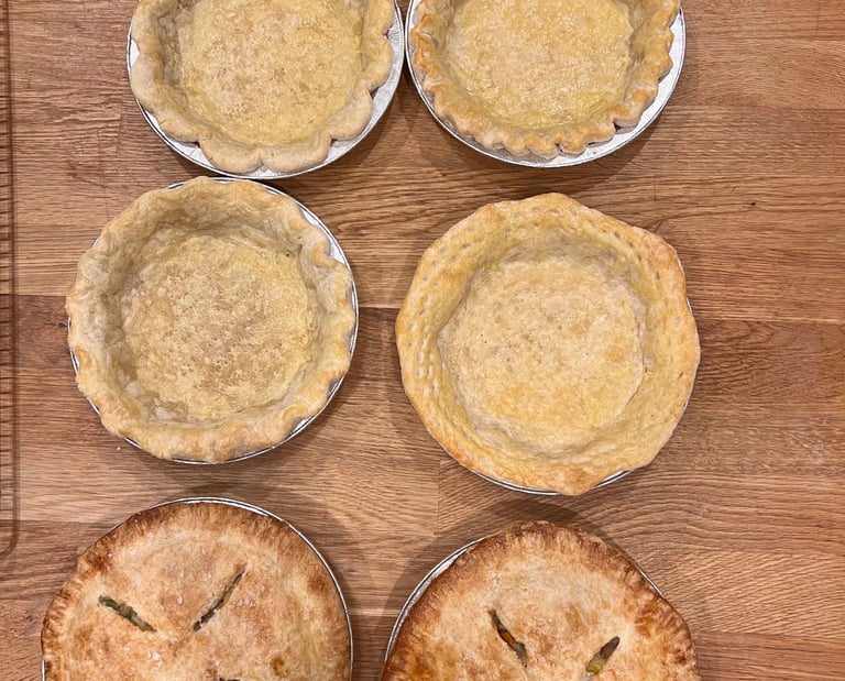 Freshly baked golden brown pie crusts and fruit pies cooling on a wooden table.