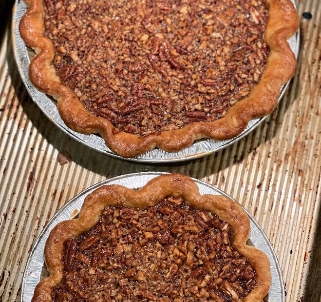 Two freshly baked pecan pies with golden fluted crusts sitting on a metal baking sheet.
