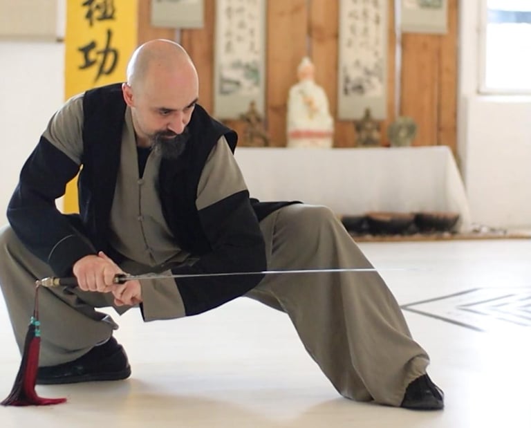 Ismet Himmet demonstrating a low Wudang sword stance (Jian) during indoor training with altar behind.