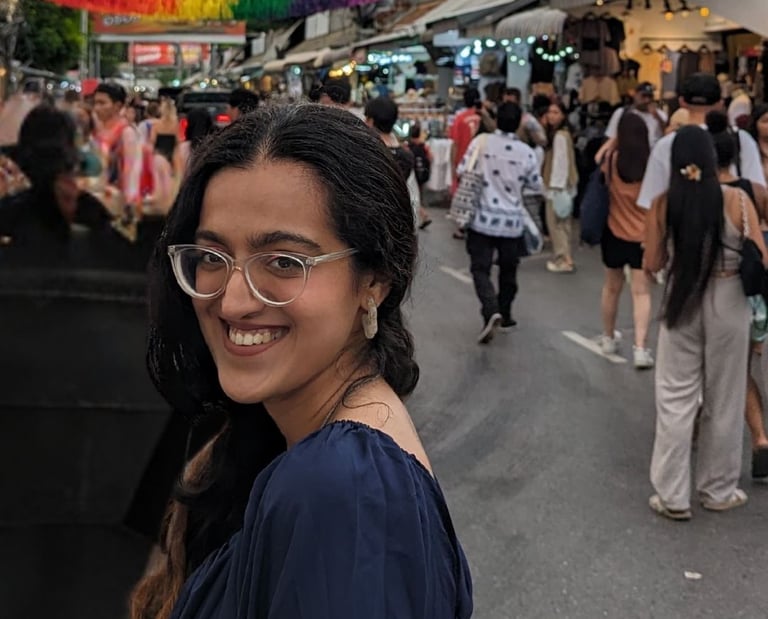 Riya, a human copywriter posing in front of an LGTBQIA+ tassel-laden market