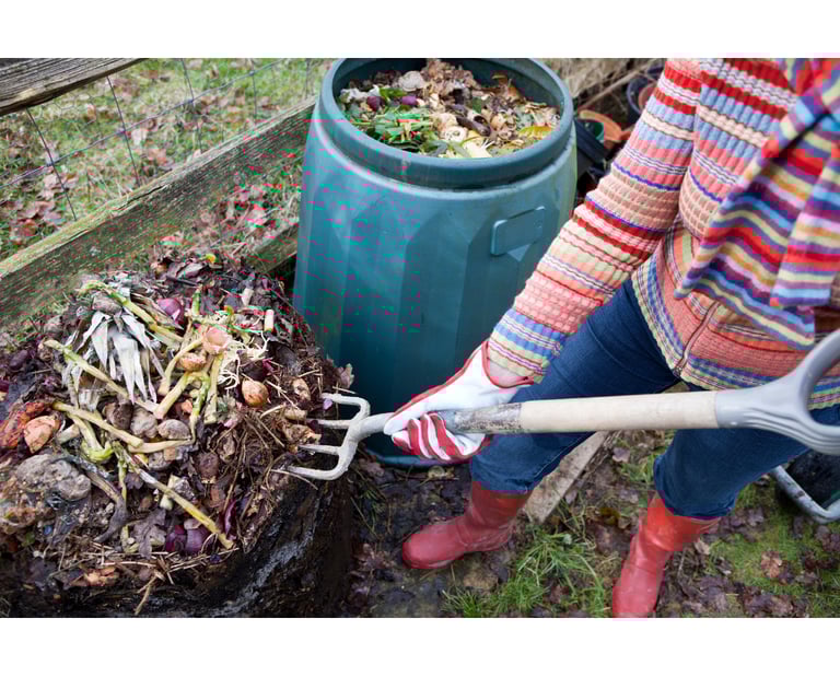 a woman turning over the compost pile