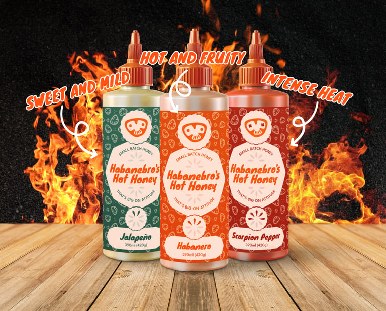 Three squeezy hot honey bottles on a wooden table, with flames in the background.