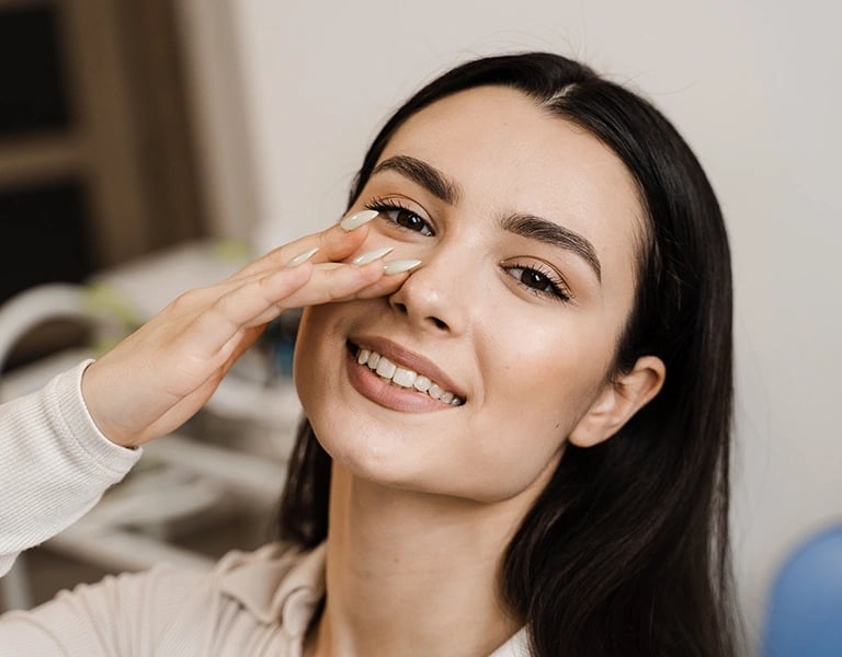 Smiling woman gently touches her nose, showing satisfaction.