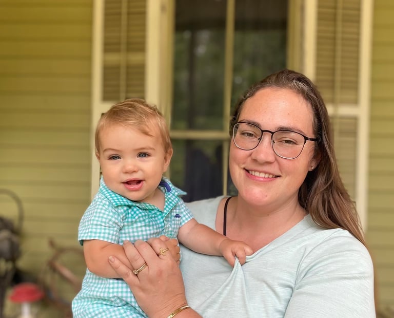 a woman in glasses and a blue shirt holding a baby