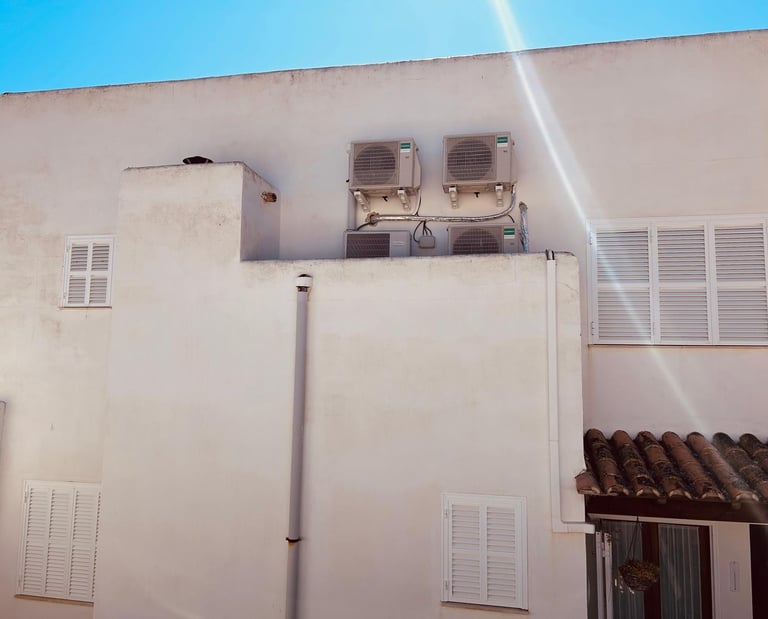 Outdoor HVAC air conditioning units mounted on a white Mediterranean building wall under a clear blue sky.