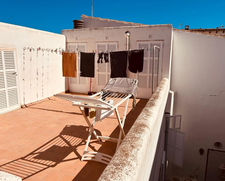 Laundry drying on a sunny Mediterranean rooftop terrace with a clothesline and folding rack.