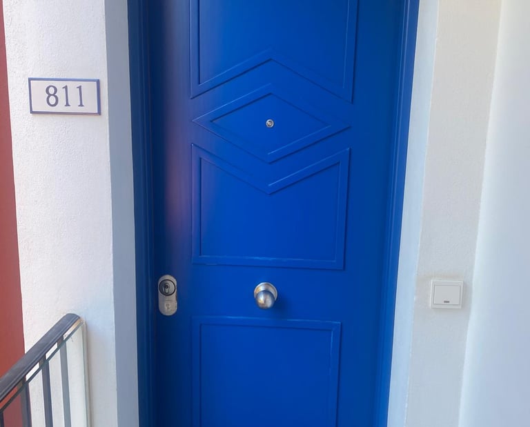 A vibrant blue front door with a geometric pattern, silver handle, and apartment number 811 on a white wall.