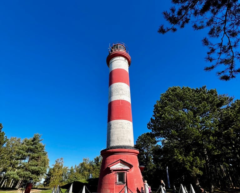 Historic Nida lighthouse tower standing tall under a clear blue sky surrounded by green trees.