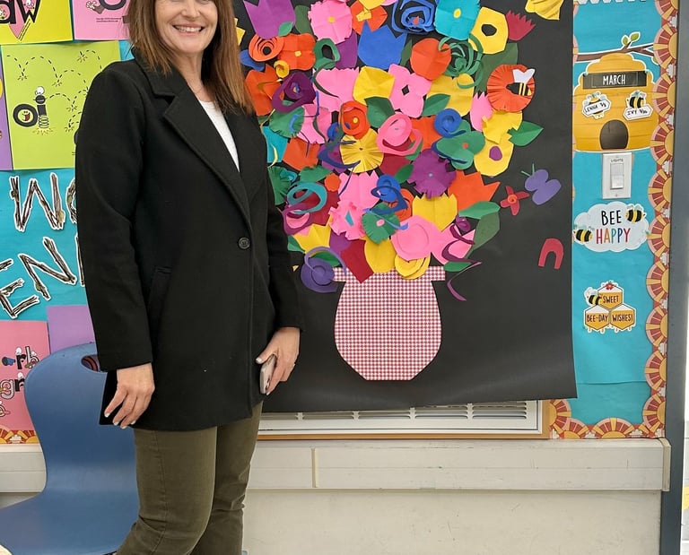a teacher standing by a collage of paper flowers