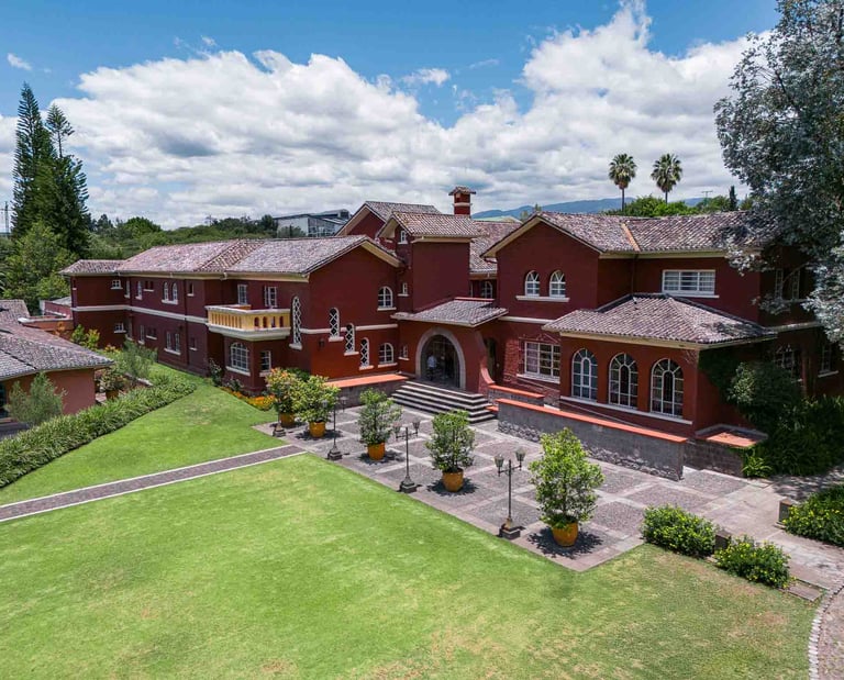 Fotografía aérea de gran casa religiosa de color rojo rodeada de hermoso  jardín verde en Quito Ecuador