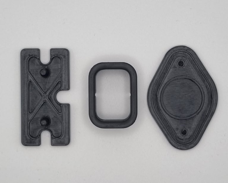 Three black 3D printed mechanical components including a bracket, spacer, and mounting plate.